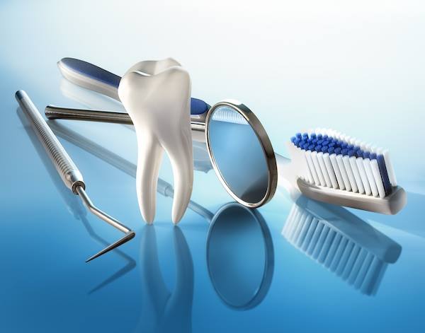 Dental mirror, model tooth, toothbrush, and instruments on a blue surface